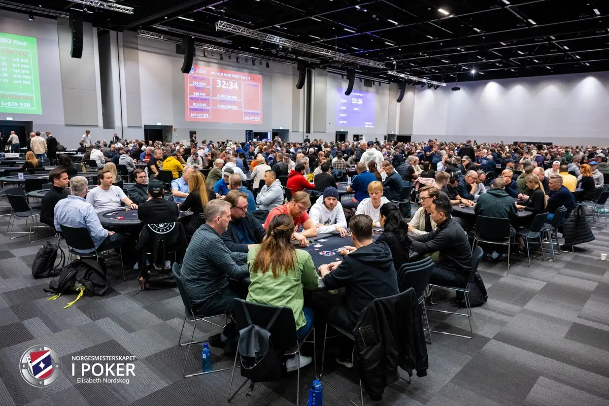 Fullsatt spillelokale under Main Event dag 1A med spillere rundt mange pokerbord og klokker på storskjerm