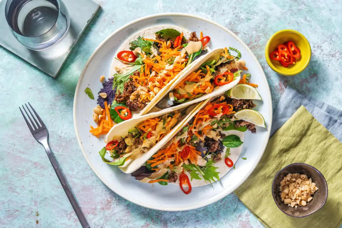 Tre tacos med kjøttdeig, revet gulrot, chili og peanøtter på en hvit tallerken