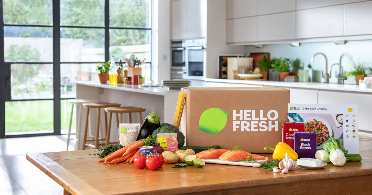 En HelloFresh-eske står på et kjøkkenbord omgitt av grønnsaker, laks og krydderposer