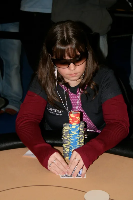 Annette Obrestad med solbriller og øreplugger sitter bak en høy stabel sjetonger ved et pokerbord