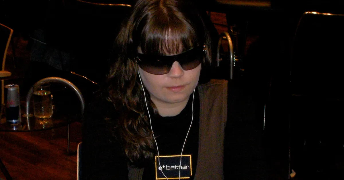 Annette Obrestad med mørke solbriller og øreplugger ved et pokerbord, med en Betfair-lapp på brystet